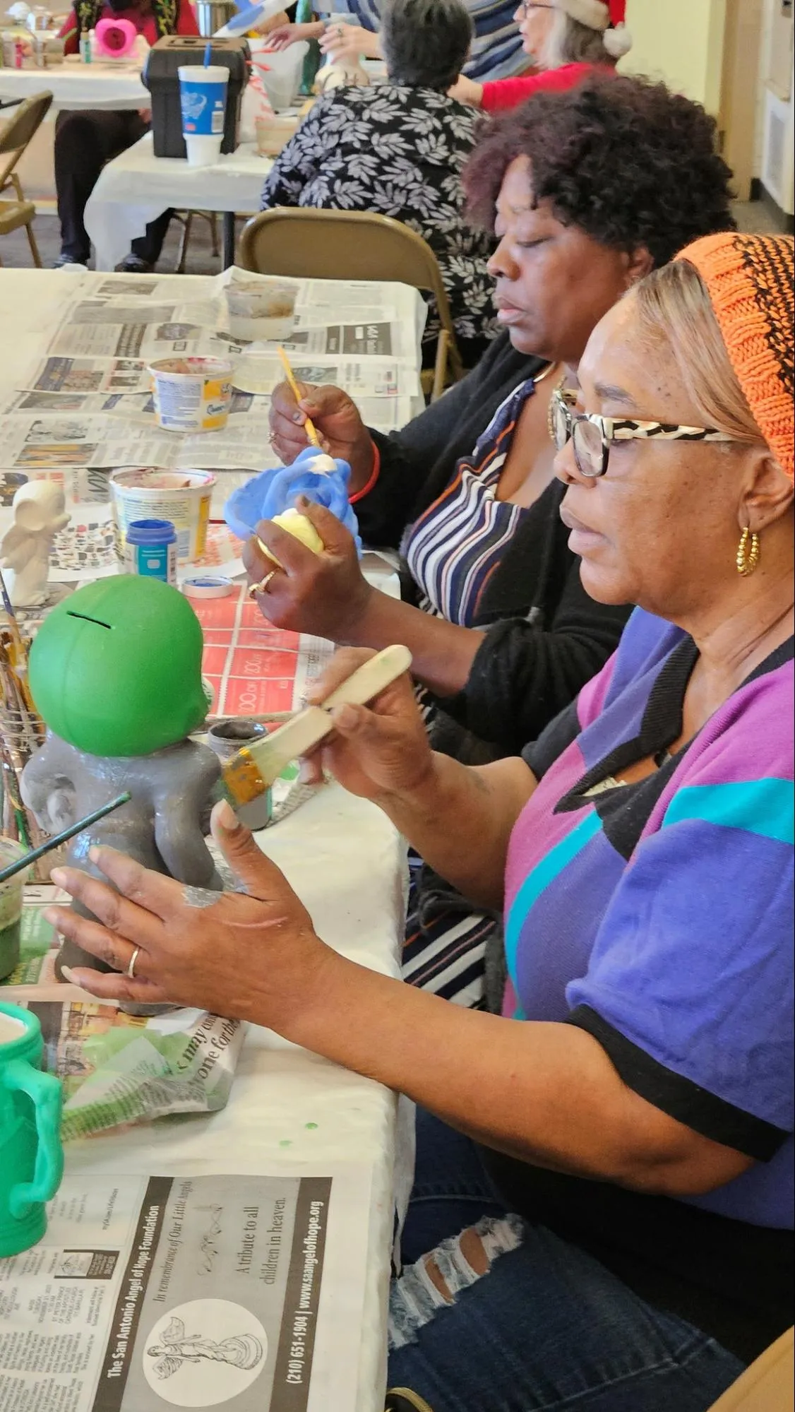 Neighbors paint ceramic pieces together at a long table