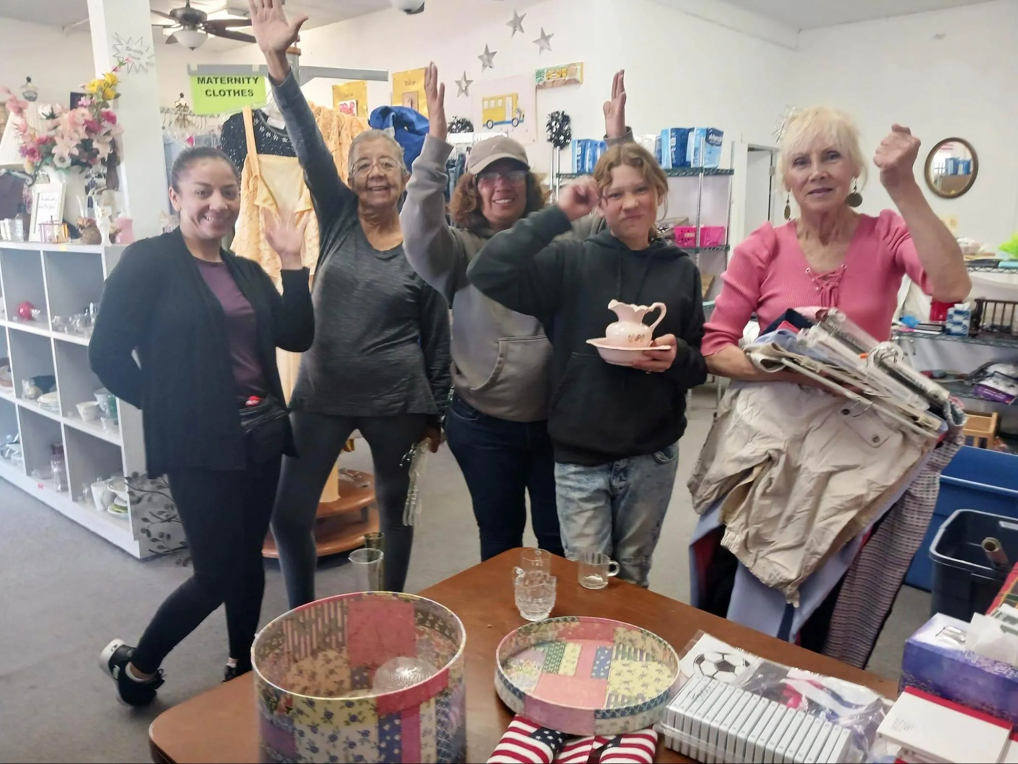 Five smiling volunteers wave from inside the HP-CAN thrift store